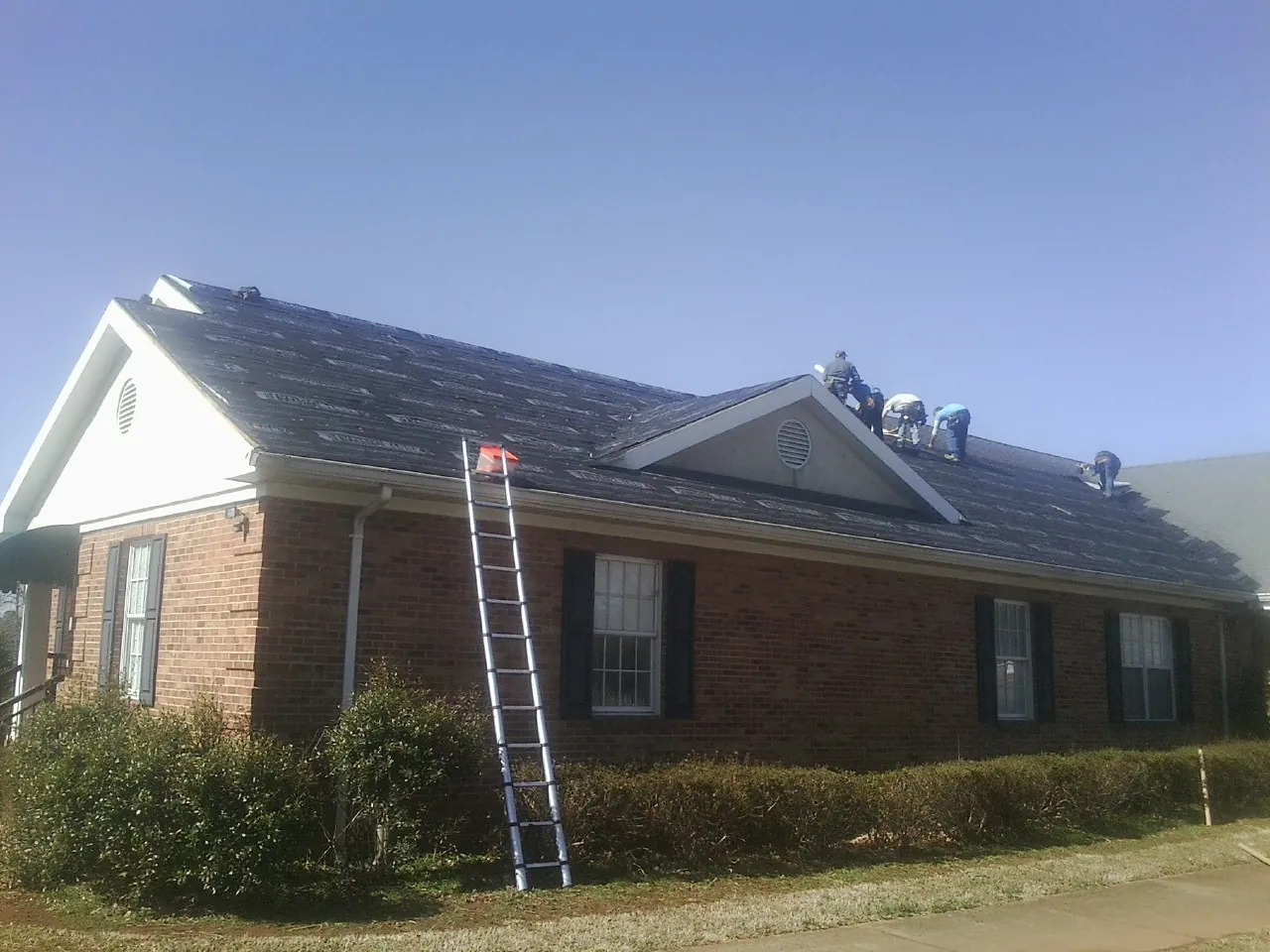 Crew tearing shingles off a brick ranch roof with a ladder set — Metal Roof Repair work by our crew in Kent